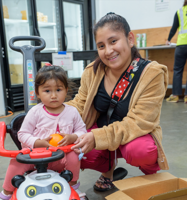 A smiling mother and daughter duo in line at the food pantry

