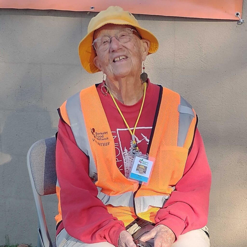 A BFN volunteer smiling in a yellow sun hat and safety vest outside the pantry